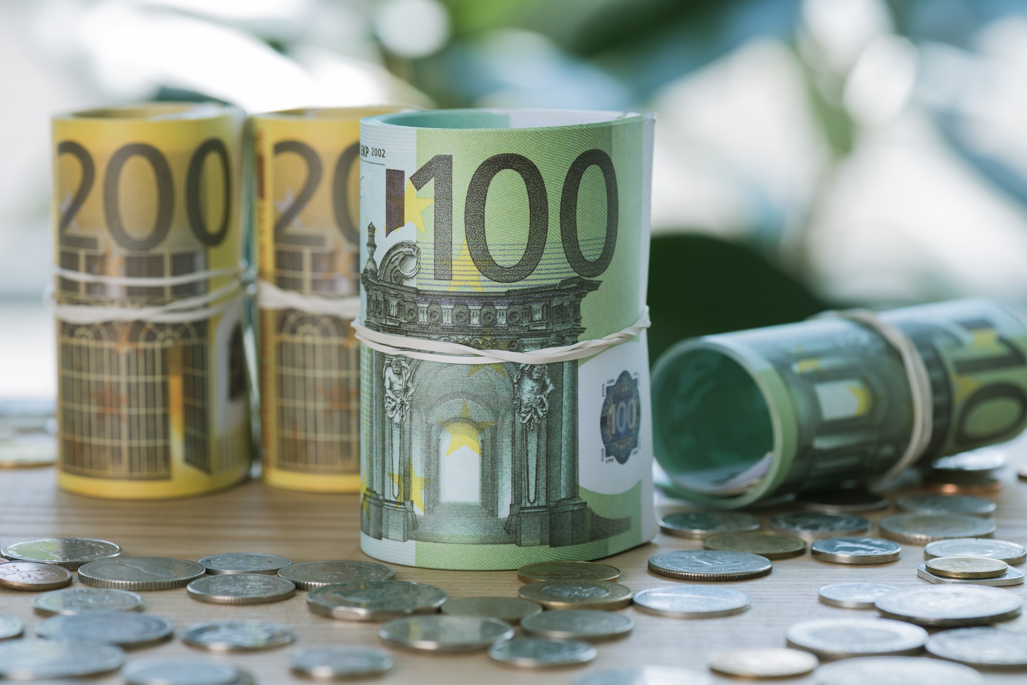 selective focus of euro banknotes in rolls with rubber bands and coins on table